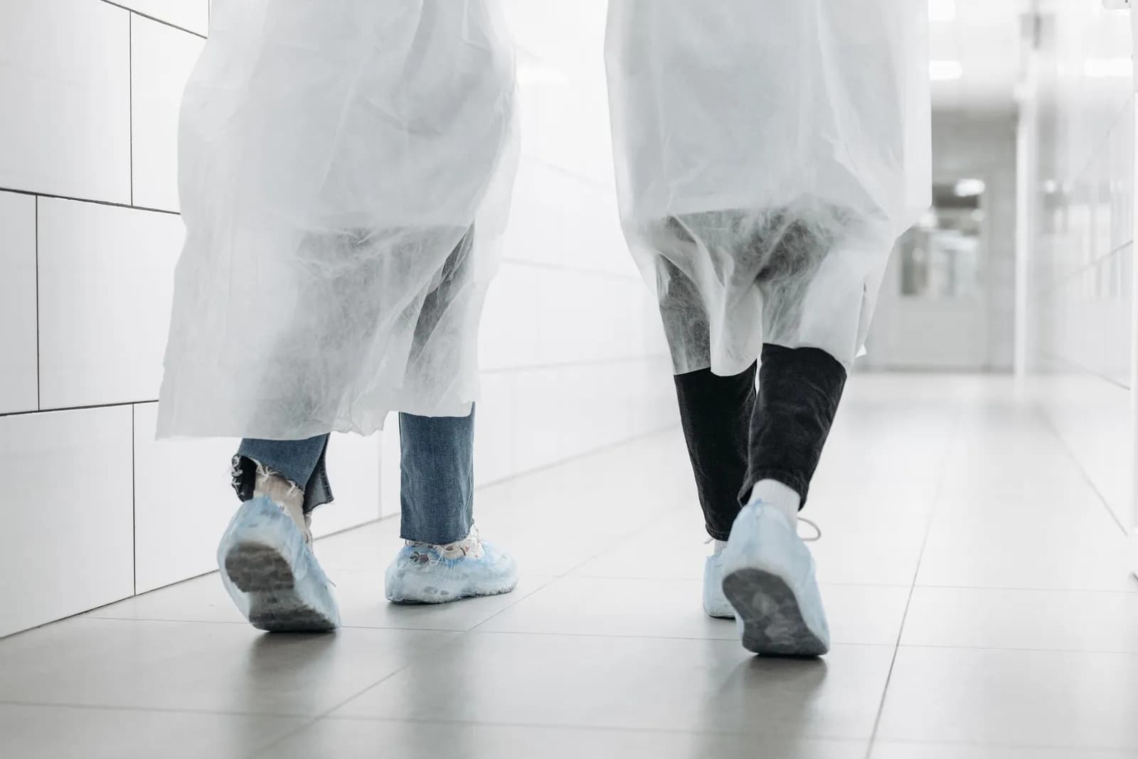 Two researchers in protective coats walking a bright laboratory corridor