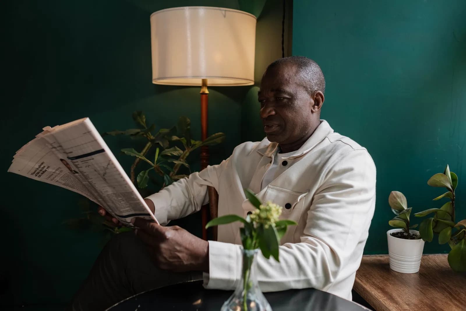 A reader with a newspaper beside a table lamp